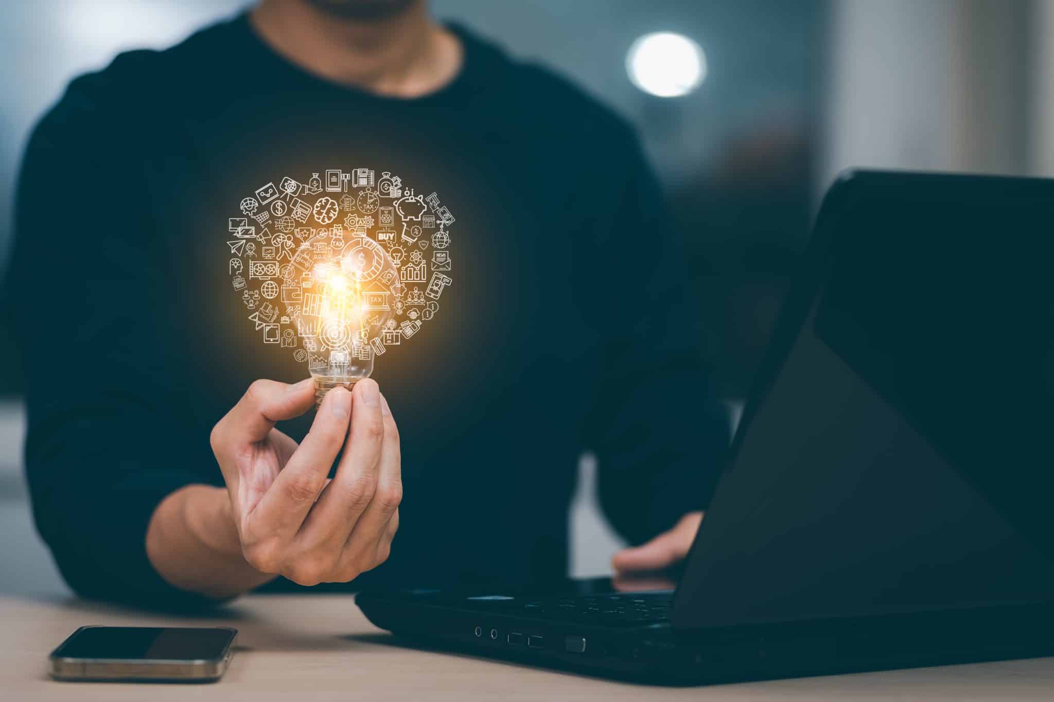 Businessman hand holding light bulb with icons and working on the desk, Creativity and innovation are keys to success.Concept of new idea and innovation with energy and power , working at home,