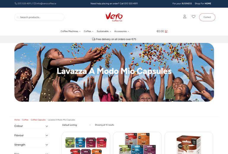 Screenshot of Vero Coffee Co's website page displaying Lavazza A Modo Mio capsules. The top banner shows a group of joyful children catching colorful objects in the air, with the product listing below featuring different coffee capsule packs. Navigation and contact info are visible.