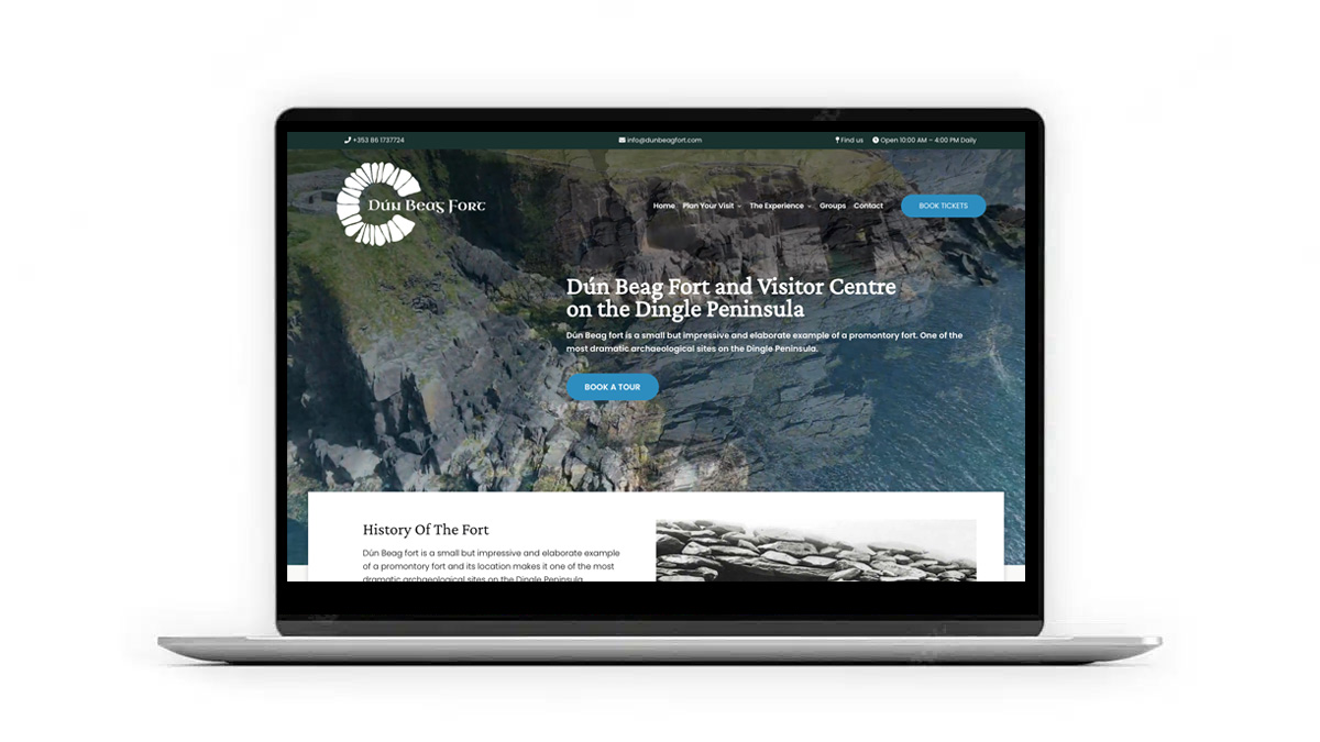 A laptop displaying a website for the Dún Beag Fort and Visitor Centre on the Dingle Peninsula. The website shows an image of a coastal cliff, the fort's name and logo, with options to book a tour and learn about the fort's history.